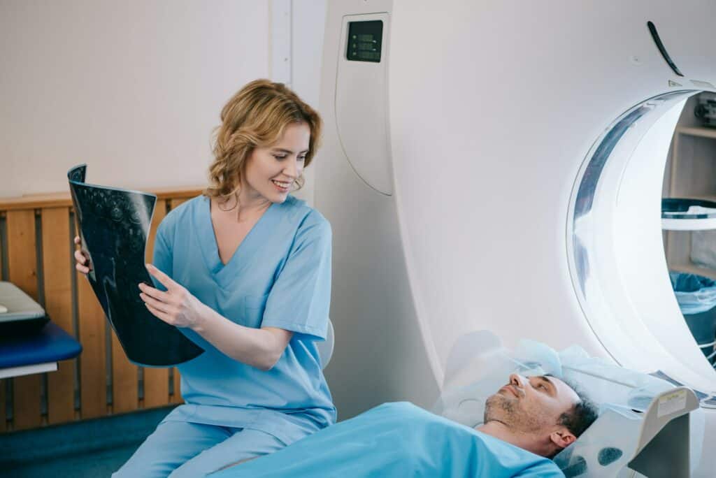 beautiful smiling doctor holding radiology diagnosis and looking at man lying on ct scanner bed