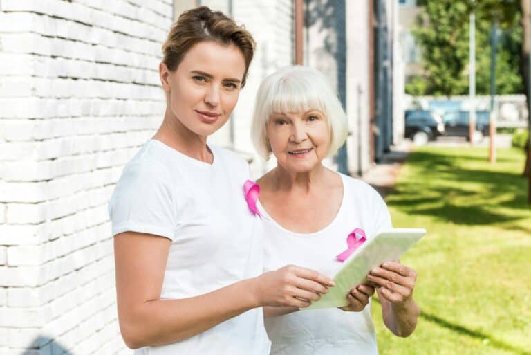 women with breast cancer awareness ribbons using digital tablet and smiling at camera